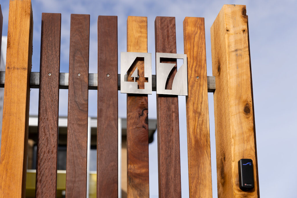 A fence of spaced wooden pails, with a metallic sign showing the address as the numeral 47.